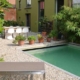 A modern small urban backyard with a gravel patio, potted plants, lounge chairs and a rectangular green swimming pool