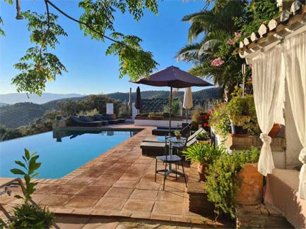 Zonnig Andalusisch cortijo met infinity zwembad, terras met parasols en uitzicht op heuvels bij Cortijo La Haza