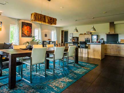 Ruime open woonkeuken met grote houten eettafel, moderne barstoelen, blauwe patroonvloer en lichte eilandkeuken