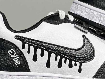 Zwarte en witte custom sneaker met druppelende Nike-swoosh en 'Eybe' merkdetail, close-up van zijaanzicht, textuur zichtbaar