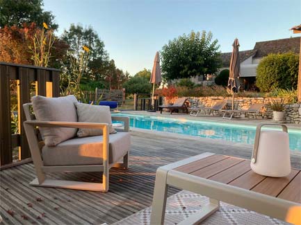 Zonnig terras met zwembad en comfortabele loungestoel bij La Ferme Buissonnière, rustieke landelijke charme en tuinzicht