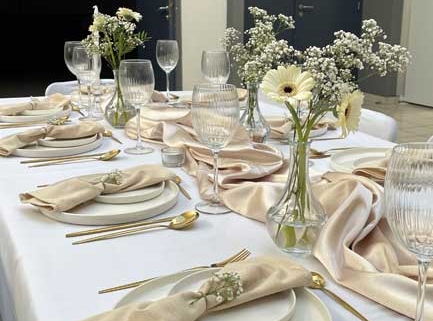 Romantic reception table with satin runner, gold cutlery, clear glassware and white gerbera and baby's breath arrangements