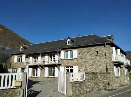Oude stenen woning "maison-fouga" in zonlicht met witte houten hekken en balkon, berglandschap op achtergrond