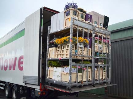 Open vrachtwagen met metalen stelling en meerdere houten kisten vol bloemen, inclusief zonnebloemen, klaar om te lossen
