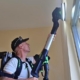 Man met rugzakstofzuiger reinigt bovenkant raam met telescoopmond in woonkamer, professionele schoonmaakapparatuur