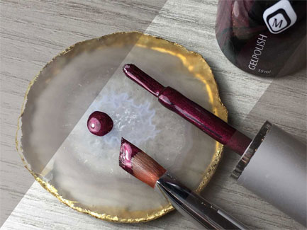 Close-up van manicure set met donkerrode gelpolish, penseel en druppel lak op agaatsteen schijf voor nagelstyling