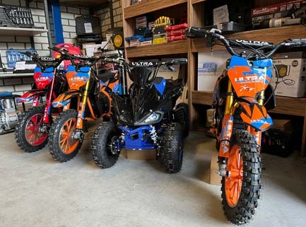 Drie offroad minibikes en een blauwe quad in garagewinkel met knobbelsbanden en felgekleurde wedstrijdstickers
