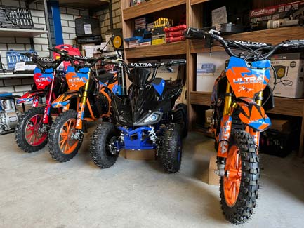 Drie offroad minibikes en een blauwe quad in garagewinkel met knobbelsbanden en felgekleurde wedstrijdstickers